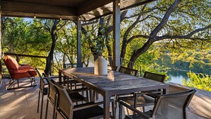 An outdoor patio with a table and chairs, surrounded by trees and a view of a lake.
