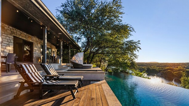 A wooden deck with lounge chairs and a pool overlooking a scenic landscape.