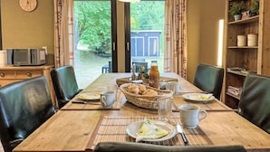 A dining area with a wooden table set for two, a microwave on a side table, and a bookshelf with books and plants. - Cosy apartment in villa for 4 people with WIFI, TV, terrace and pets allowed (Bad Wildungen)