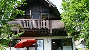 A two-story wooden house with a balcony, a red umbrella, and a table with chairs outside. - Cosy apartment in villa for 4 people with WIFI, TV, terrace and pets allowed (Bad Wildungen)