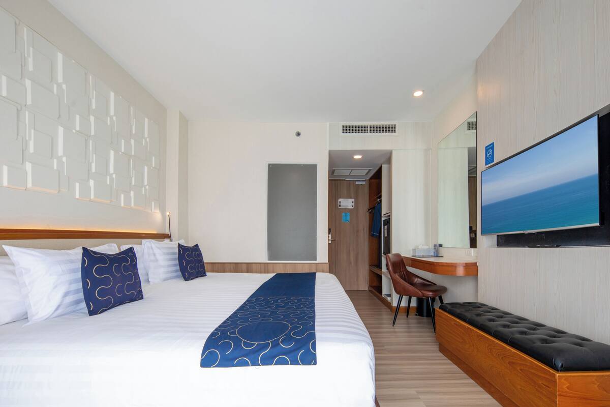 A hotel room with a large bed, a TV, a desk, and a seating area.