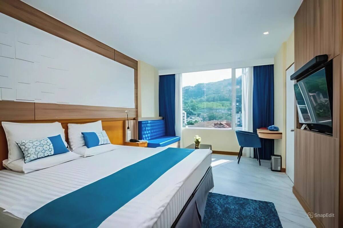 A hotel room with a large bed, a desk, a TV, and a view of the outdoors.