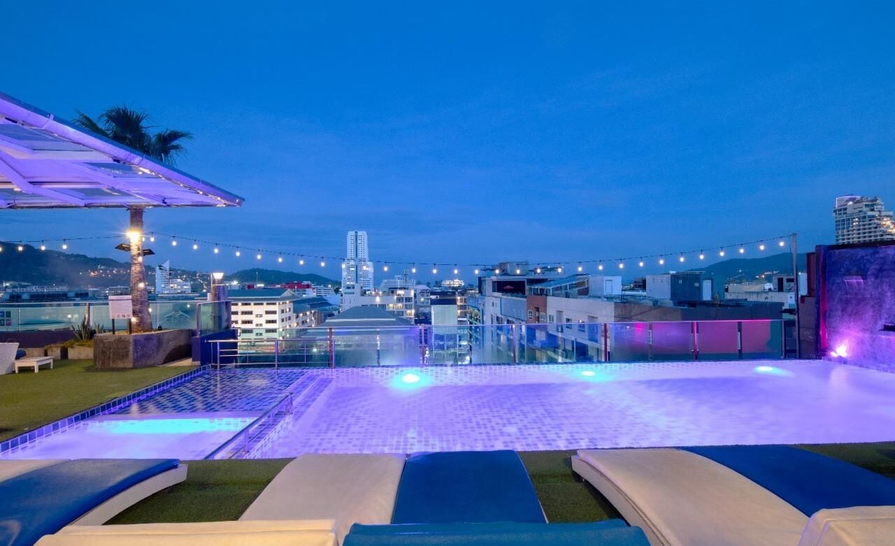 A rooftop pool with lounge chairs, string lights, and a cityscape view in the background.