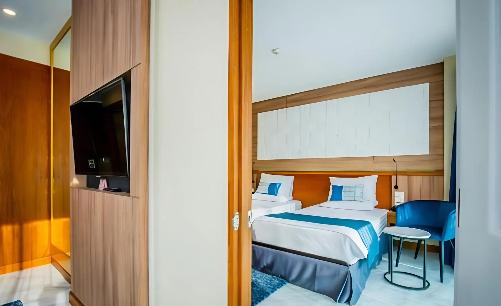 Ein Hotelzimmer mit Bett, Schreibtisch, Stuhl und einem an der Wand befestigten Fernseher.