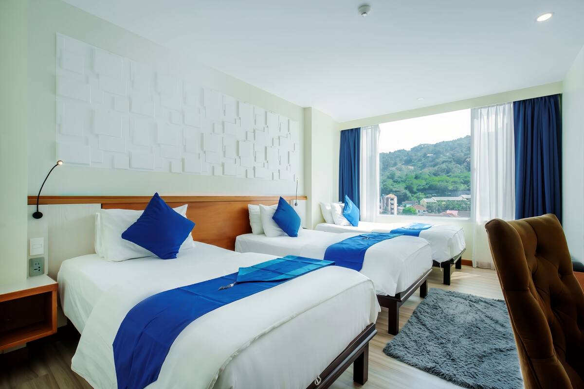 A hotel room with two beds, a large window with a view, a headboard with a light fixture, and a brown chair.