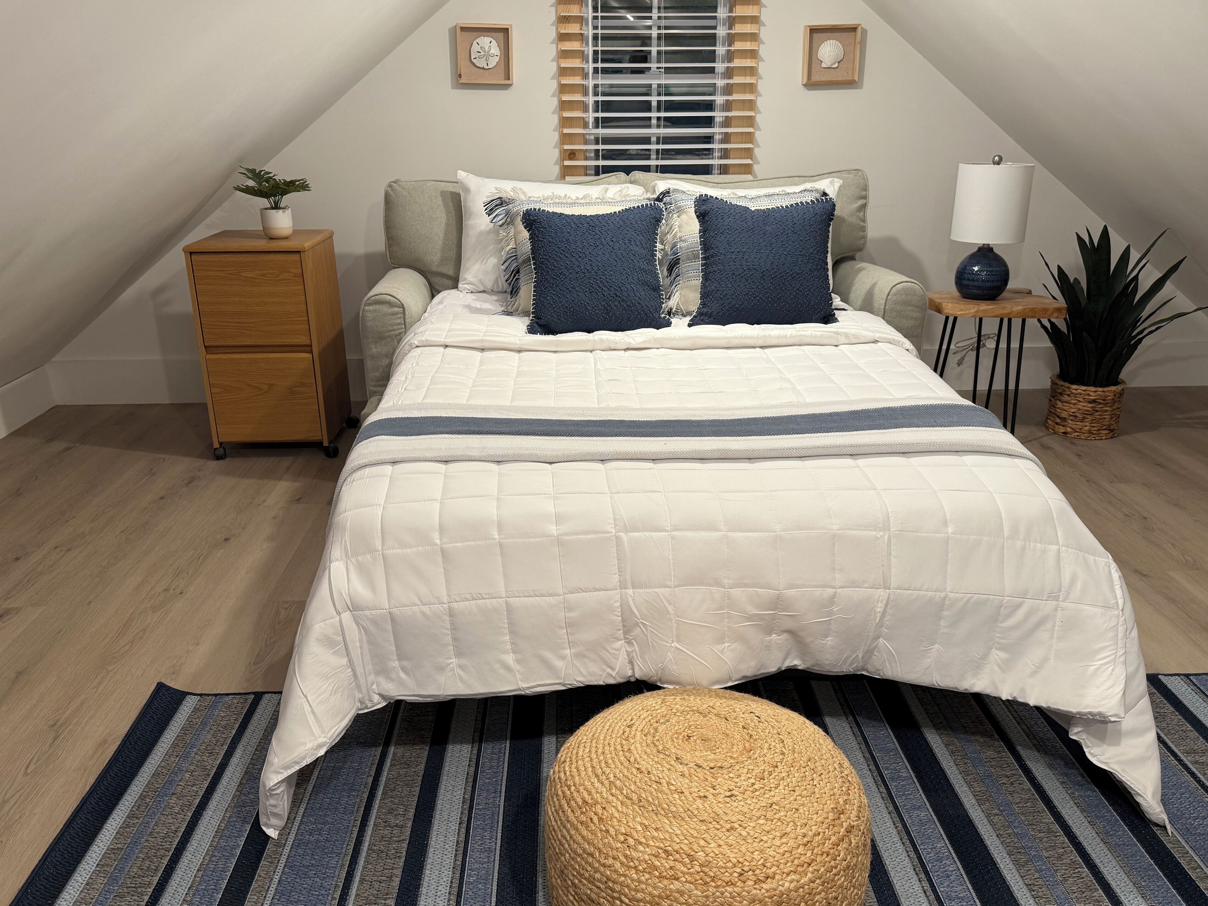Un dormitorio con cama, mesita de noche, lámpara y planta en maceta.