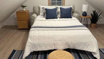 Un dormitorio con cama, mesita de noche, lámpara y planta en maceta.