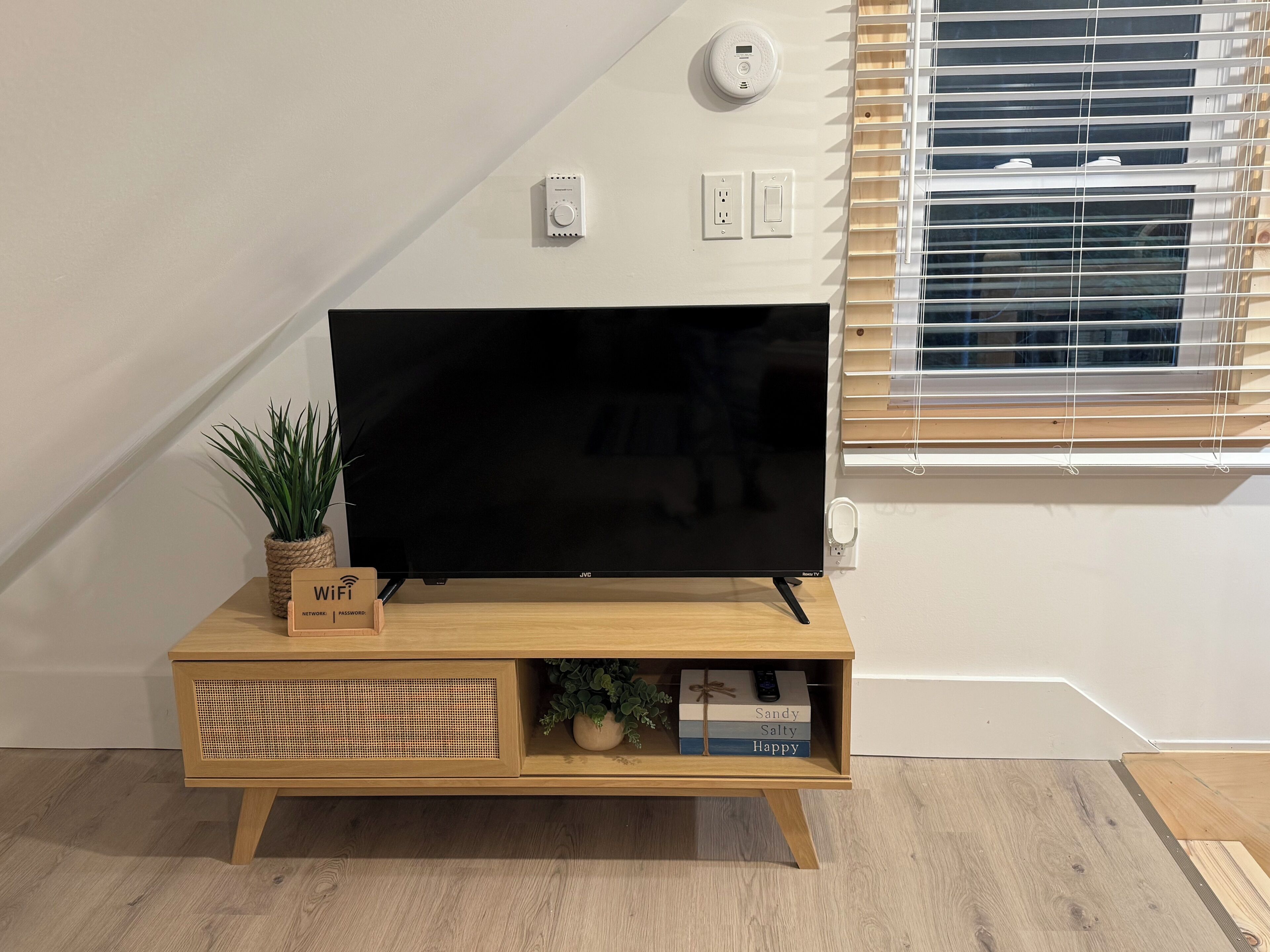 En platt-TV placerad på ett TV-bord i trä, med en växt och en Wi-Fi-symbol bredvid.