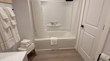 Ein Badezimmer mit einer Badewanne, einer Toilette und einem Waschbecken. Handtuchhalter mit gefalteten Handtüchern, eine Duschvorhang und eine kleine Ablage mit Toilettenartikeln.