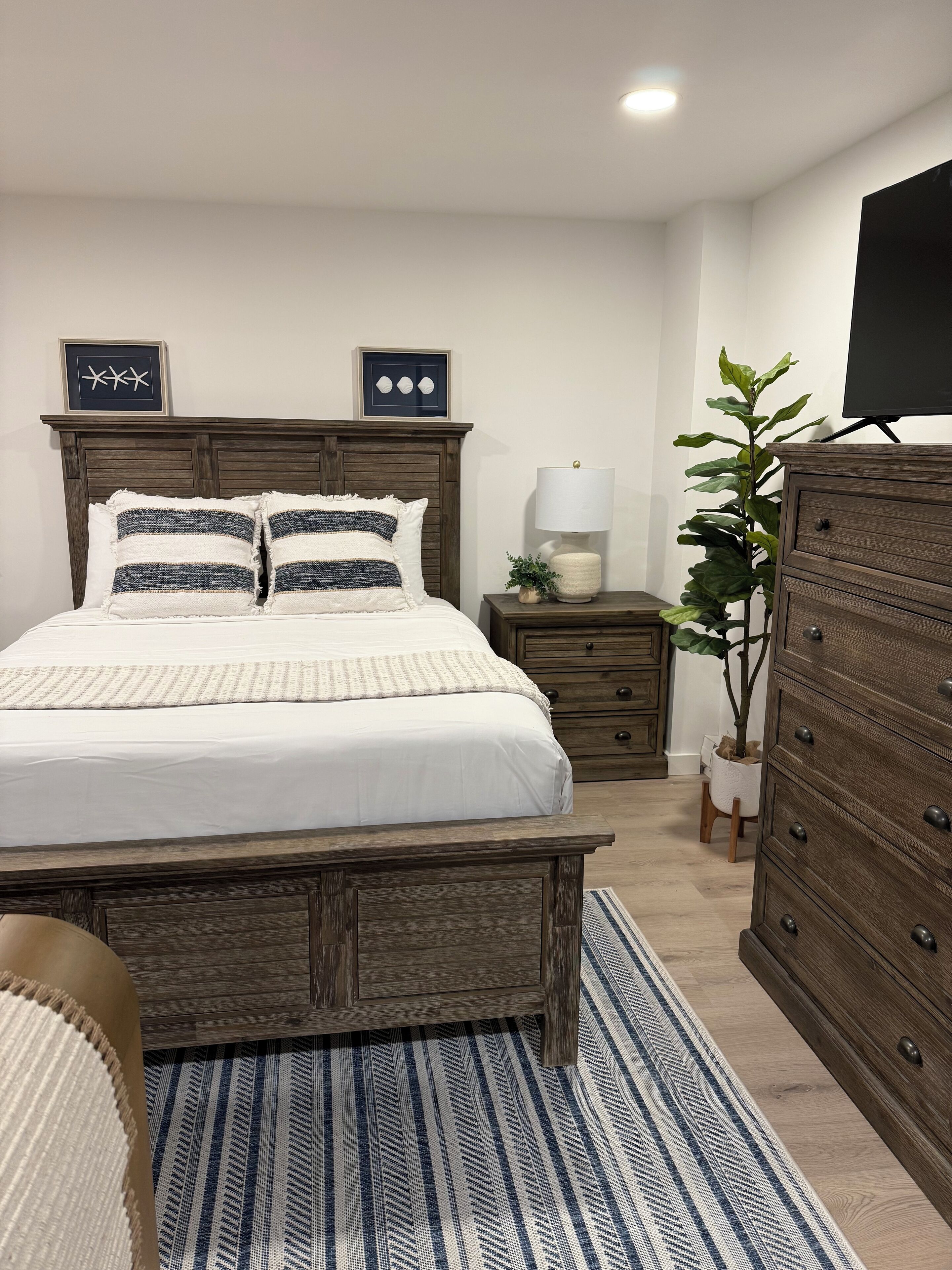 Een slaapkamer met een houten bed, nachtkastjes, een dressoir en een kamerplant.
