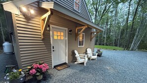 A house with a gravel driveway, a front door, and two Adirondack chairs outside.