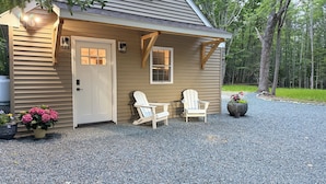 A cozy cabin with a gravel driveway, two Adirondack chairs, and a potted plant.