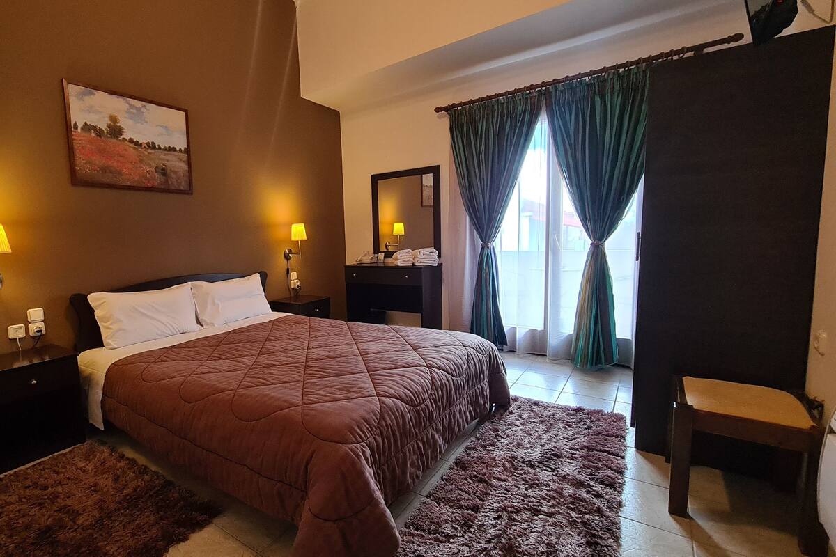 Habitación de hotel con cama, dos lámparas de noche, teléfono, espejo y ventana con cortinas.