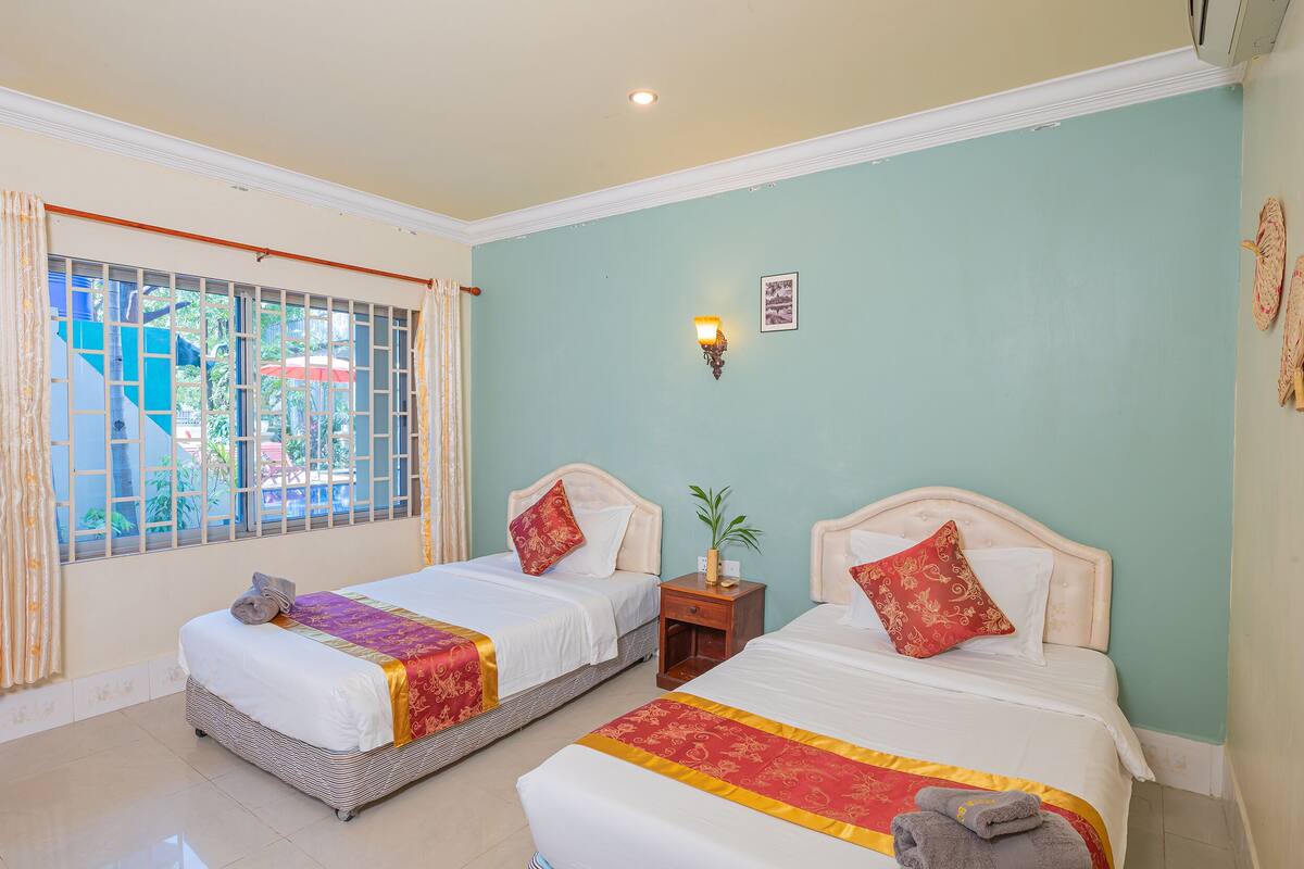 A hotel room with two beds, a window with a view, a nightstand, and a wall-mounted light.