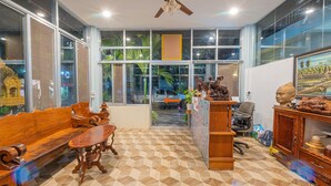 A spacious room with a large wooden bench, a small table, and a ceiling fan. - Lotus Bleu Guest House (Siem Reap)