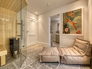 A modern bathroom with a glass shower enclosure, a sauna, and a cozy seating area with cushions.