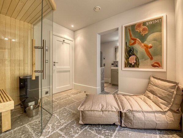A modern bathroom with a glass shower enclosure, a sauna, and a cozy seating area with cushions.