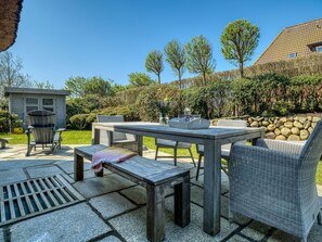 An outdoor patio area with a wooden table and chairs, a small shed, and a stone wall.