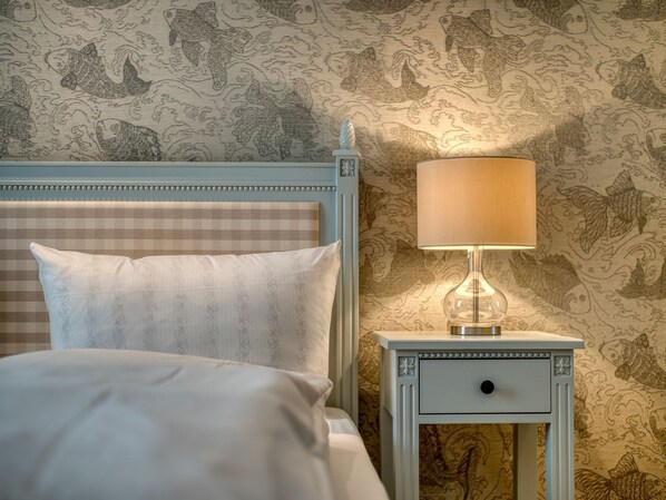 A neatly made bed with a checkered headboard, a bedside table with a lamp, and a wall with a detailed fish pattern.