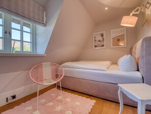 A bedroom with a bed, a chair, a small table, and a window with curtains.