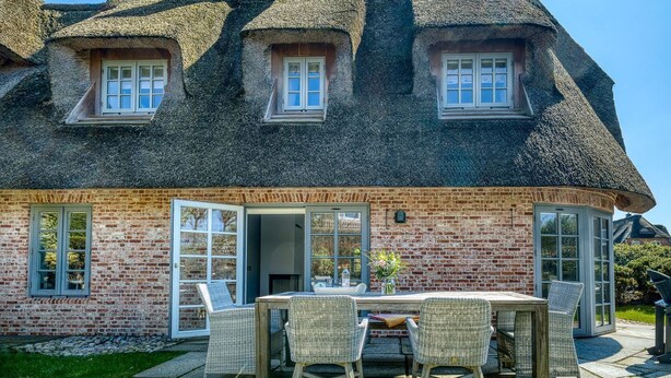 Una casa in mattoni con tetto di paglia, un'area pranzo con mobili in vimini e un camino in mattoni.