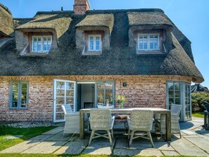 A brick house with a thatched roof, a dining area with wicker furniture, and a brick chimney.