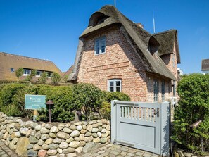 A traditional brick building with a thatched roof, a stone wall, and a metal gate.