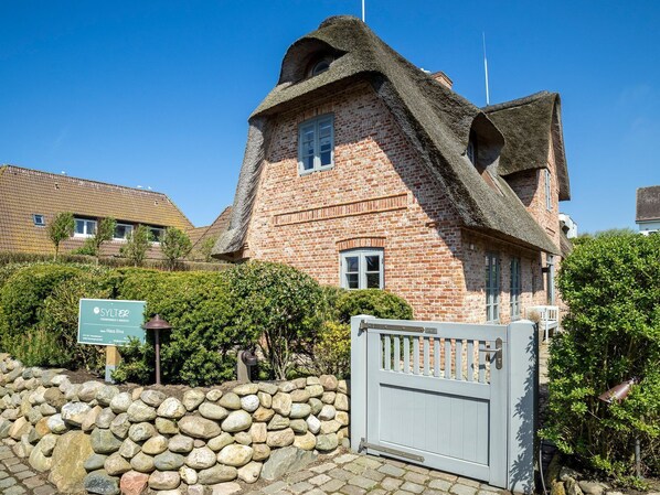 A traditional brick building with a thatched roof, a stone wall, and a metal gate.