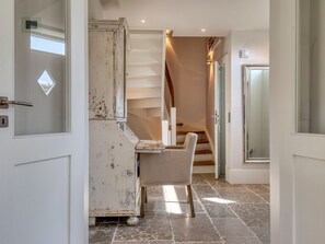 A hallway with a staircase, a white door with a glass panel, and a chair.