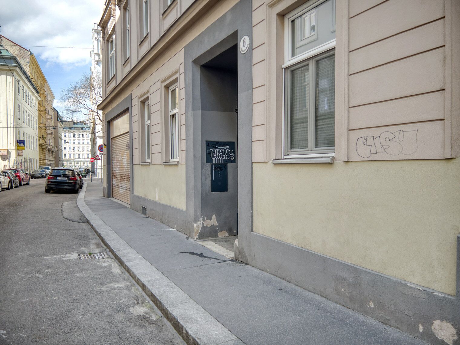 A street view of a building with a closed garage door, a sign with graffiti, and a number '6' on the wall.