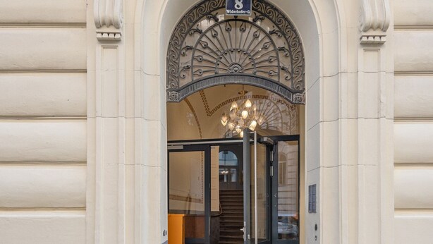 An entrance with an ornate metal archway, a sign indicating room number 8, and a modern glass door. - Cool Alsergrund 1BR, Fully Equipped, by Blueground (Vienna)