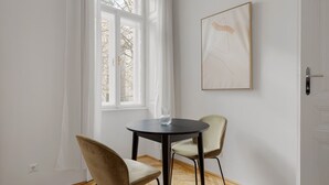 A room with a round table and two chairs, a window with white curtains, and a framed abstract painting on the wall. - Cool Alsergrund 1BR, Fully Equipped, by Blueground (Vienna)