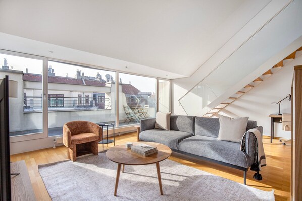 Relax in a spacious living room with a city view, featuring a sofa, armchair, and staircase.