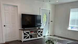 A living room with a flat-screen TV, a ceiling fan, a white door, a stained glass window, and a large plant. - Newly renovated home walkable to Downtown/Restaurants/Park (Ukiah)