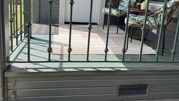 A porch with a green railing, a white door, and a wicker chair.