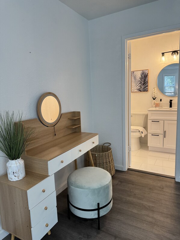 A bathroom with a wooden vanity, a round mirror, a small stool, and a wicker basket.