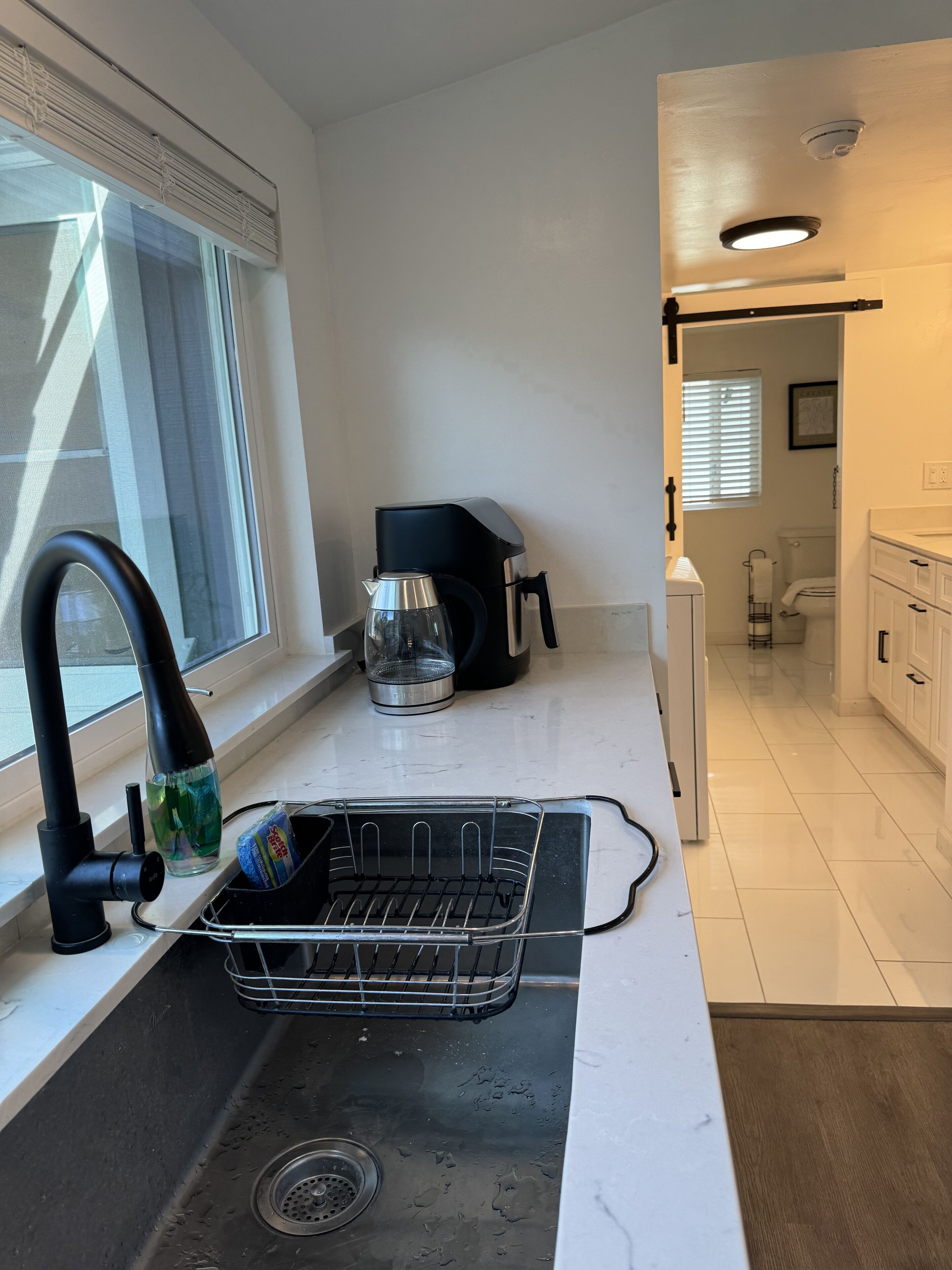 Una cocina moderna con un lavamanos de acero inoxidable, una cafetera y un escurreplatos.