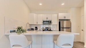 Una cocina moderna con armarios blancos, un refrigerador de acero inoxidable, un microondas y una isla central con dos taburetes de bar.