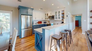 A modern kitchen with white cabinets, a stainless steel refrigerator, a microwave, and a large island with bar stools. - Shared Pool, Boardwalk to the Beach, Pet Friendly (Port Aransas)