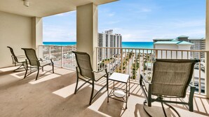 Un balcone con tre sedie e un tavolino, vista sulla spiaggia e sullo skyline della città.