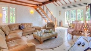 Amplia sala de estar con un sofá seccional grande, una mesa de centro de vidrio y una escalera de madera.