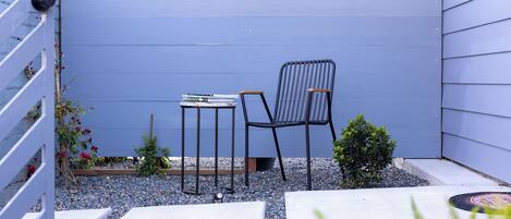 Un petit espace extérieur aménagé avec une table et deux chaises, entouré de gravier et de petites plantes.