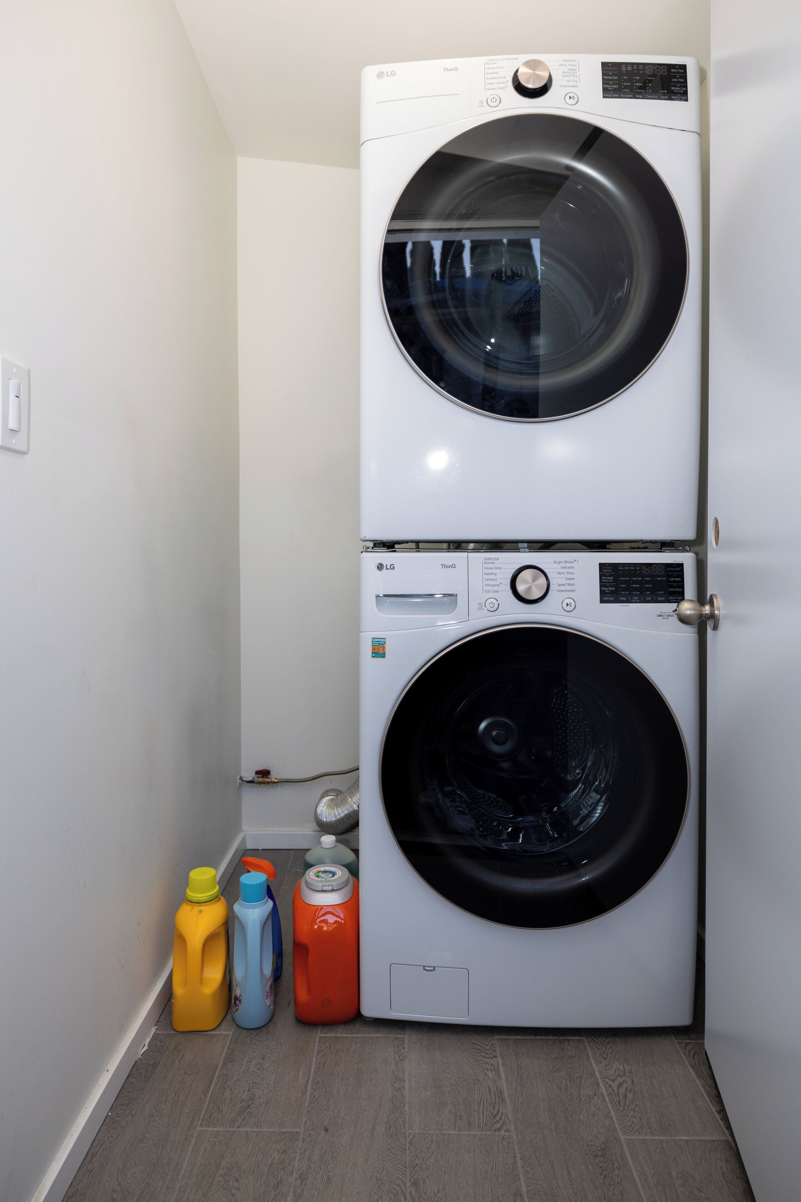 A laundry room with two stacked front-loading washing machines and three detergent bottles.