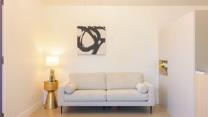 A modern living room with a light-colored sofa, a gold side table with a lamp, and a large abstract painting on the wall. - Hollywood Family Nest in Burbank, Steps to Studios! (Burbank)