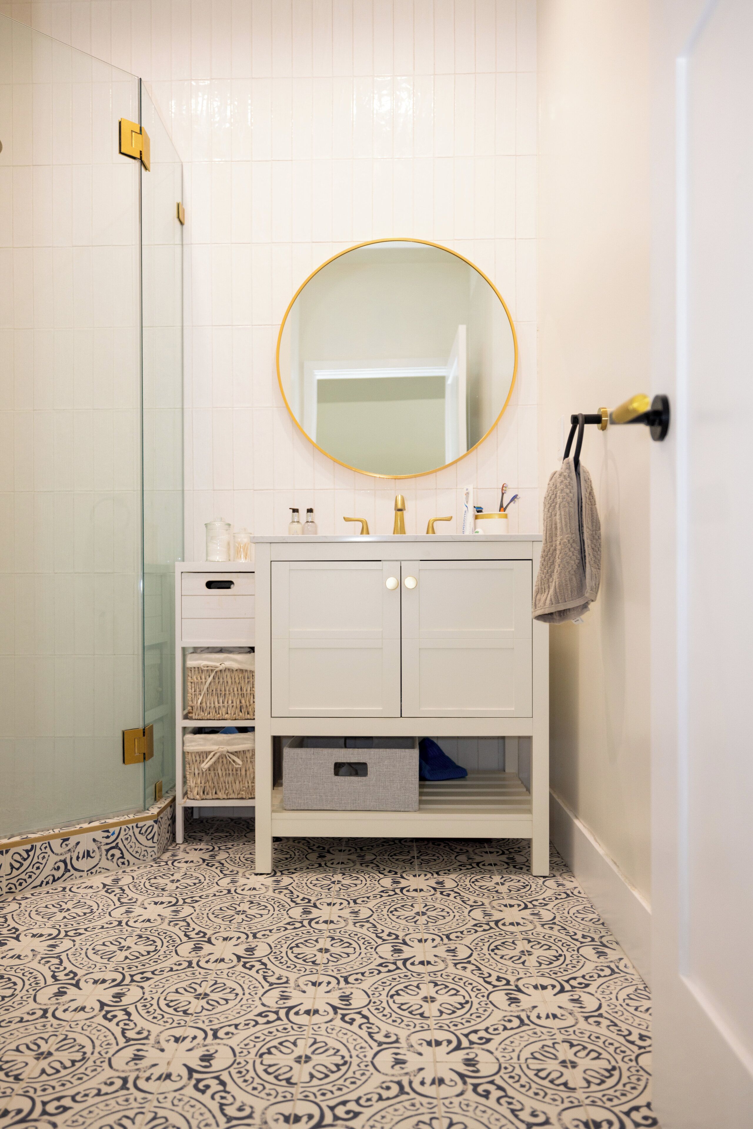 Une salle de bain avec un meuble-lavabo blanc, un miroir rond et des carreaux de sol à motifs.