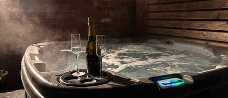 A hot tub with two glasses and a bottle of champagne, surrounded by wooden walls and string lights.