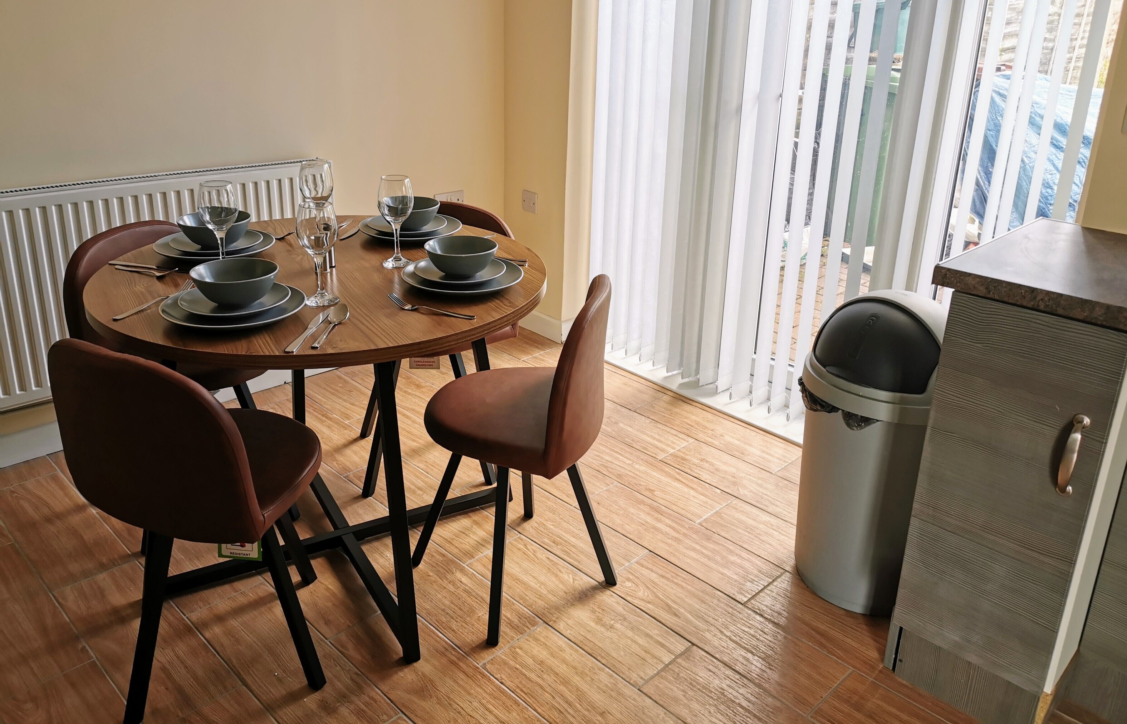 A dining area with a round table, four chairs, and a trash bin.