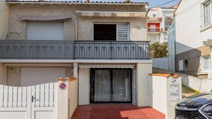 Edifici de dues plantes amb entrada tancada per una reixa, un balcó i un cotxe aparcat.