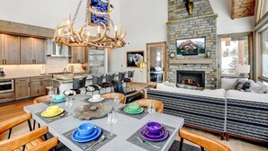 A spacious living area with a fireplace, dining table set for six, and a large stone fireplace above the sofa.