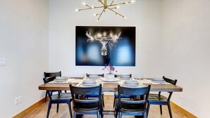 Zona pranzo con un lampadario moderno, un grande quadro astratto e un tavolo in legno apparecchiato per quattro persone.